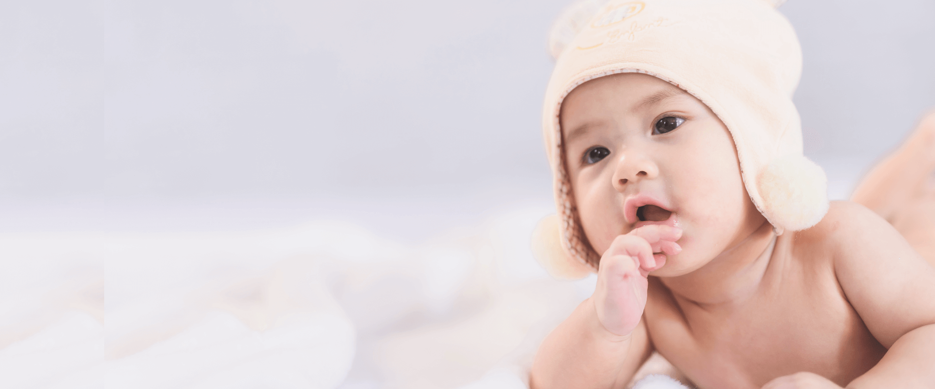 foto de bebê oriental de bruços com uma das mãos na boca em fundo azul